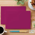 Bold berry magenta blank submission card with envelope, pen, coffee, stamps, plant on wood desk.